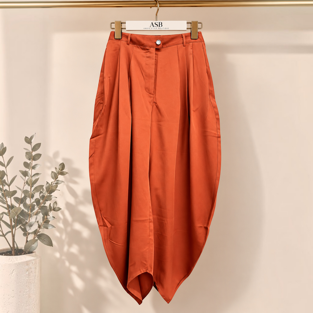 Angie Style Boutique rust orange high-waisted balloon pants with front and back pleats hanging on a clothing rack