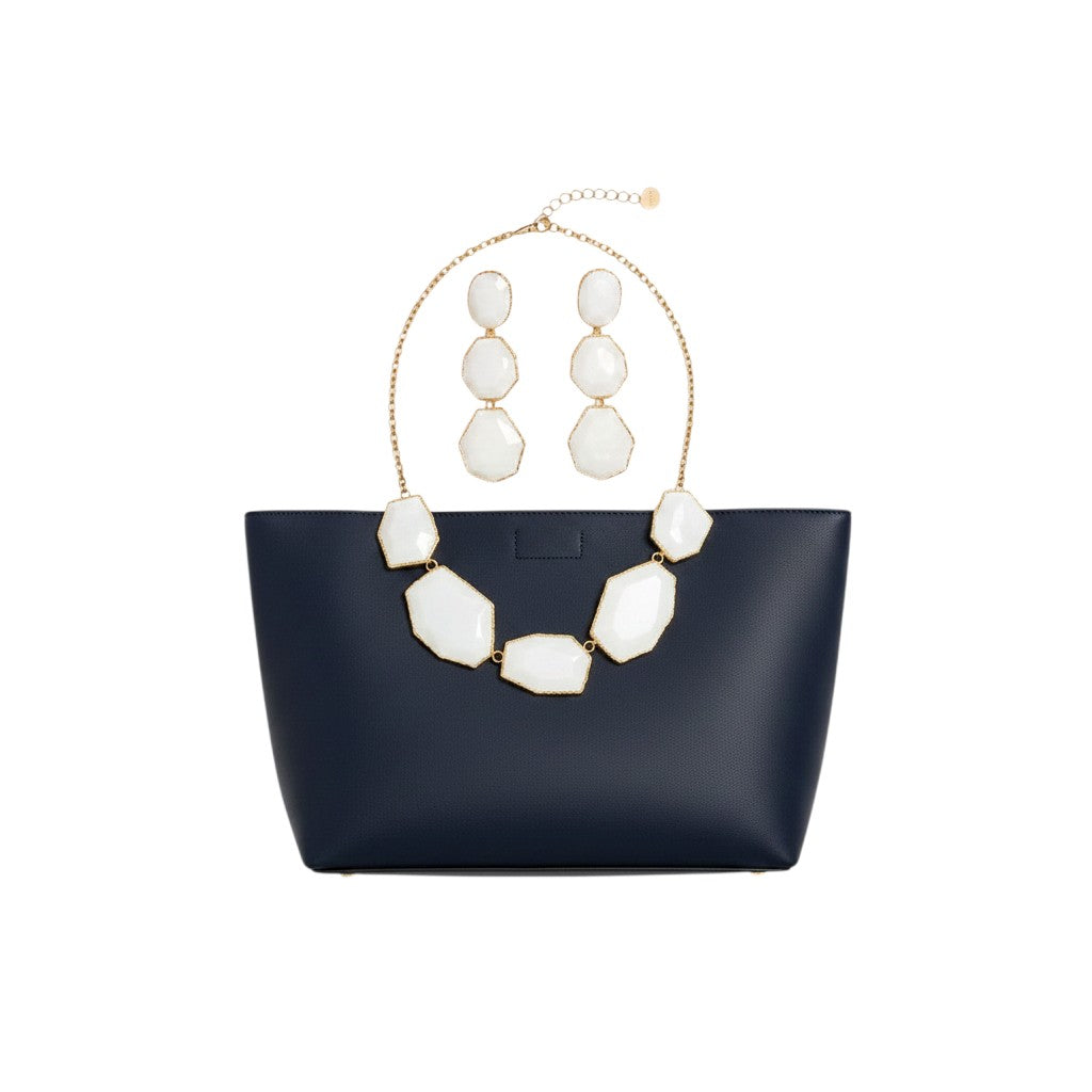 Angie Style Boutique white geometric stone statement necklace and tiered drop earring set displayed on a navy tote bag.