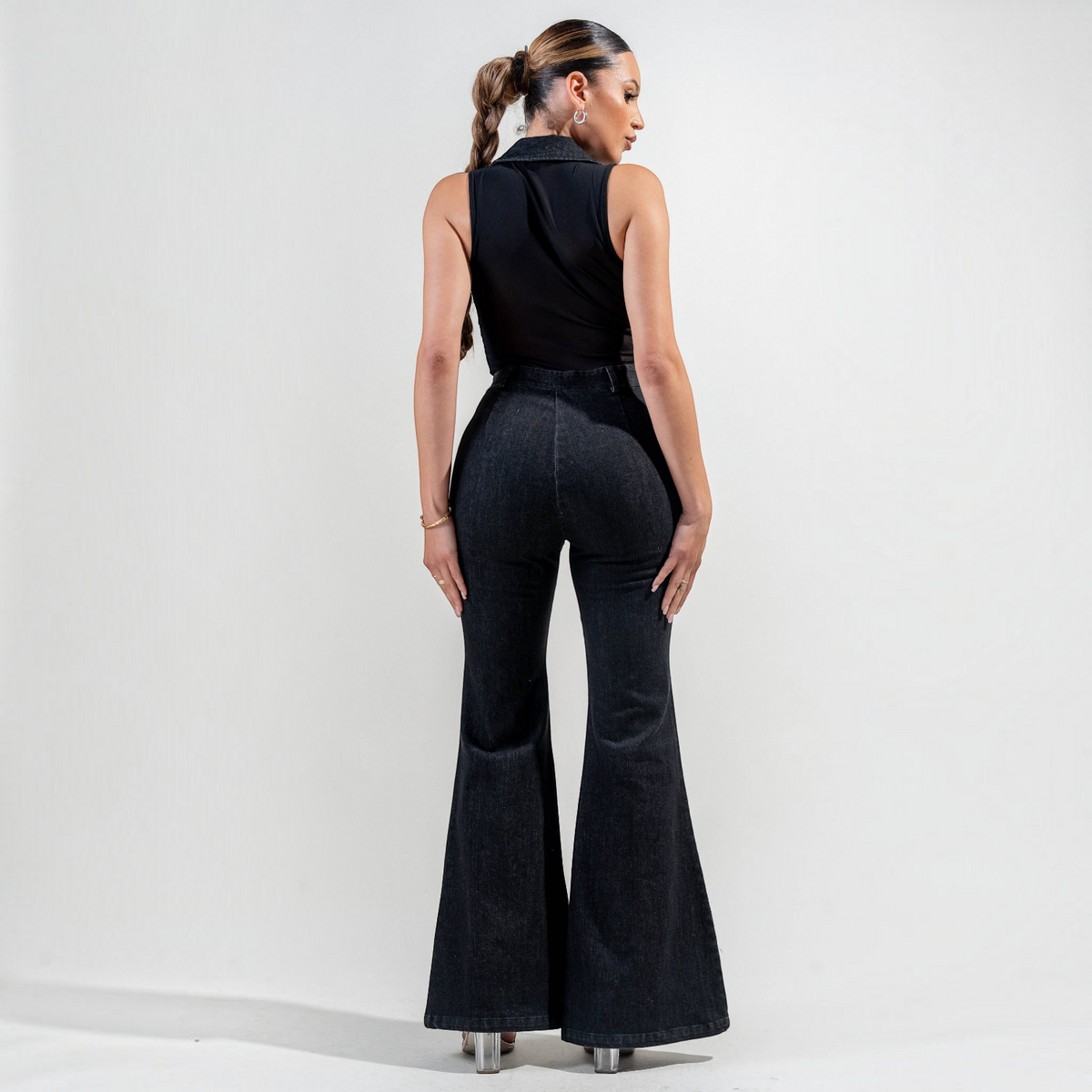 Model wearing an Angie Style Boutique black stretch washed denim and mesh jumpsuit with a flared leg, back view.